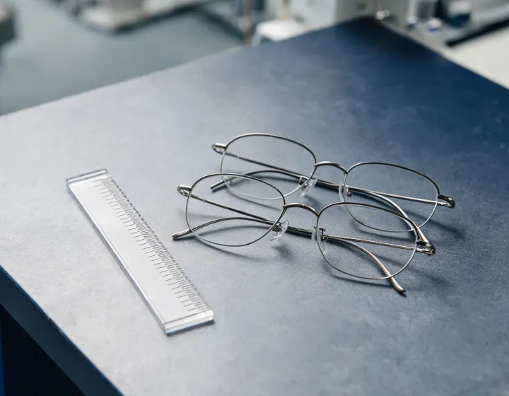 Unlabeled flexible memory-metal eyewear frames on an optical packing bench, application sketch only